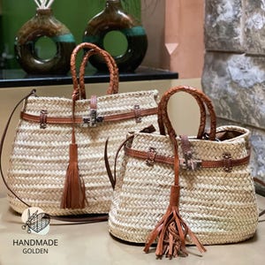 Peut inclure: Deux sacs à main en paille tressée avec des détails en cuir marron. Les sacs ont des poignées en cuir tressé, des lanières en cuir et des glands décoratifs. Les sacs sont étiquetés "HANDMADE GOLDEN".