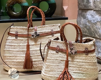 Puede incluir: Dos bolsos de mano de paja tejida con detalles de cuero marrón. Los bolsos tienen asas de cuero trenzado, correas de cuero y borlas decorativas. Los bolsos están etiquetados como "HANDMADE GOLDEN".
