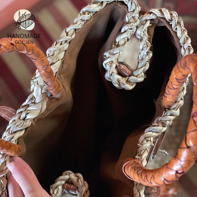 Puede incluir: Bolso tote Handmade Golden. El bolso presenta un dise&ntilde;o de paja tejida con bordes trenzados y asas de cuero. El interior est&aacute; forrado con una tela marr&oacute;n. El bolso tiene una est&eacute;tica natural y terrosa.