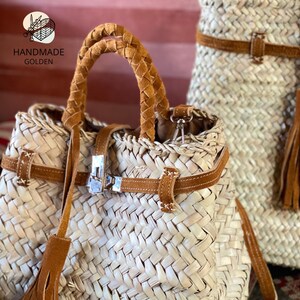 May include: Woven straw handbags with brown leather accents. The bags feature braided handles, leather straps, and metal clasps. One bag has a tassel. The text "HANDMADE GOLDEN" is visible.