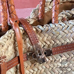 Puede incluir: Primer plano de un bolso de mano de paja tejida con detalles de cuero marr&oacute;n. El bolso tiene un cierre plateado y asas de cuero trenzado. Las palabras "HANDMADE GOLDEN" est&aacute;n impresas en el bolso.