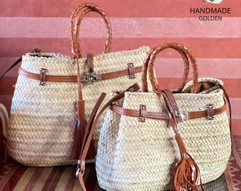 Puede incluir: Dos bolsos de mano de paja tejida con detalles de cuero marrón. Los bolsos tienen asas trenzadas, correas de cuero y borlas decorativas. Los bolsos son de diferentes tamaños, el más grande en el fondo y el más pequeño en primer plano. Los bolsos están etiquetados "HANDMADE GOLDEN".