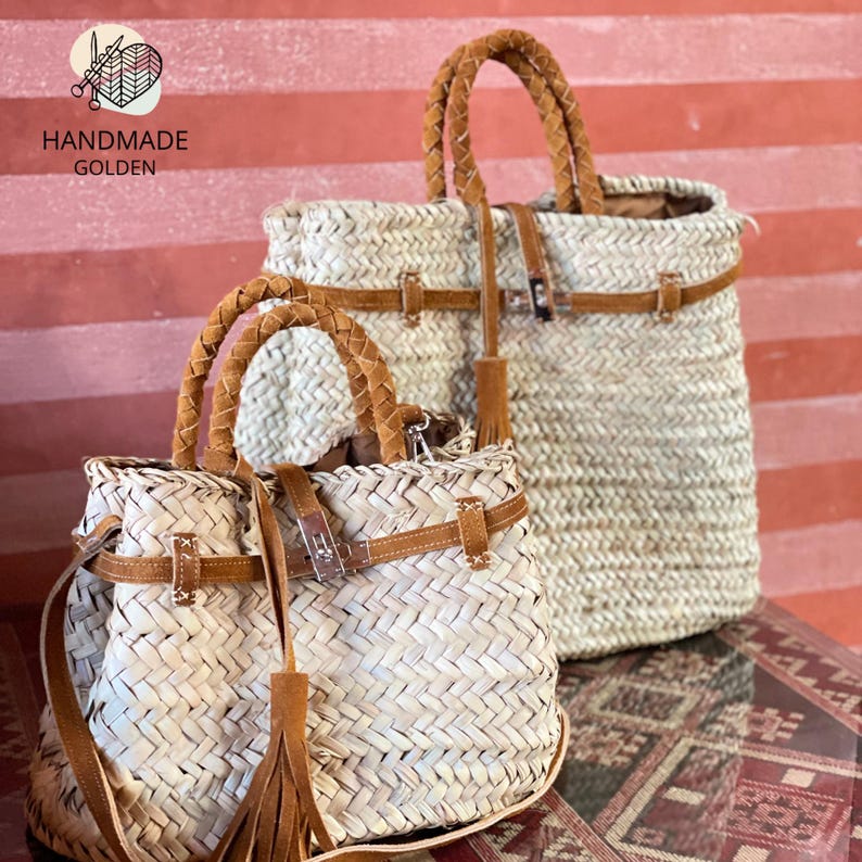May include: Two woven straw handbags with brown leather accents. The bags have braided handles, leather straps, and decorative tassels. The text "HANDMADE GOLDEN" is visible in the upper left corner.