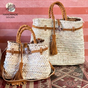 May include: Two woven straw handbags with brown leather accents. The bags have braided handles, leather straps, and decorative tassels. The smaller bag has a shoulder strap. The text "HANDMADE GOLDEN" is visible.