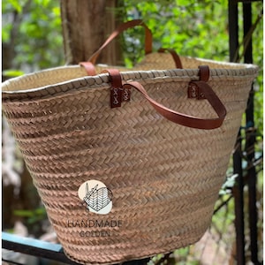 Peut inclure: Un sac fourre-tout en paille tressée avec des poignées et des accents en cuir marron. Le sac a une large ouverture et une construction robuste. Le sac porte une étiquette indiquant "HANDMADE GOLDEN".