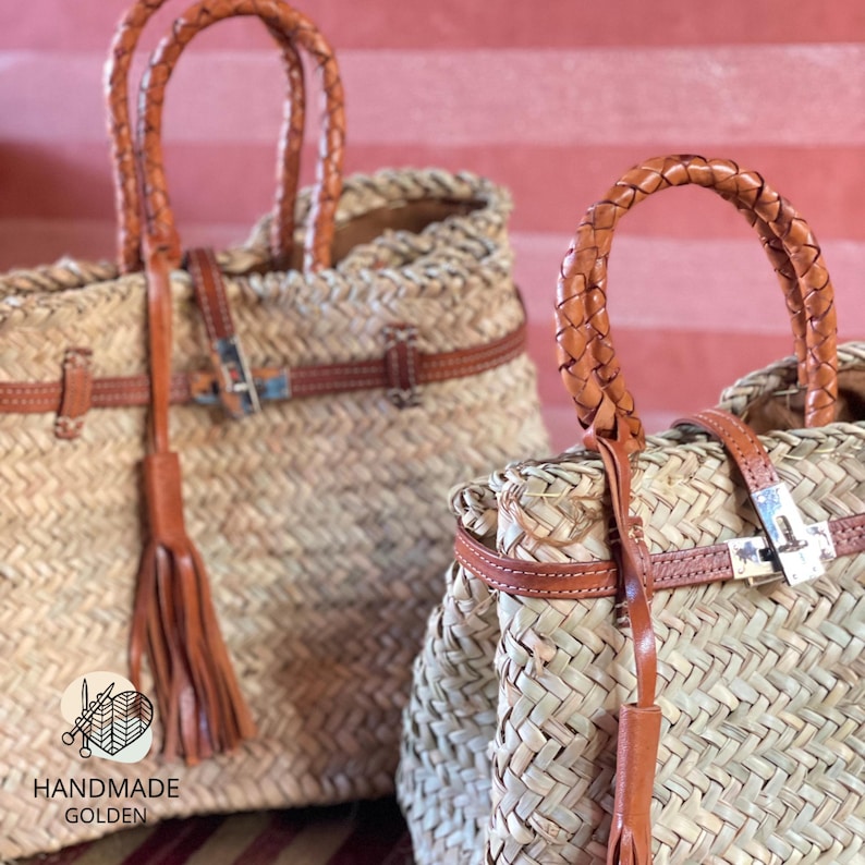 Puede incluir: Dos bolsos de mano de paja trenzada con detalles de cuero marr&oacute;n. Los bolsos tienen asas de cuero trenzado, correas de cuero con hebillas plateadas y borlas de cuero. Los bolsos son hechos a mano, como indica el texto "HANDMADE GOLDEN".