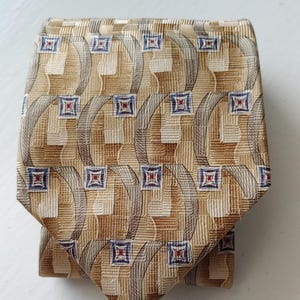 May include: A beige silk tie with a geometric pattern of brown, blue, and red squares. The pattern is repeated throughout the tie.