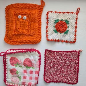 May include: Four handmade pot holders in various designs. One is orange with an owl, another has a red rose on white, a third features strawberries, and the last is red and white knitted. Each has a loop for hanging.