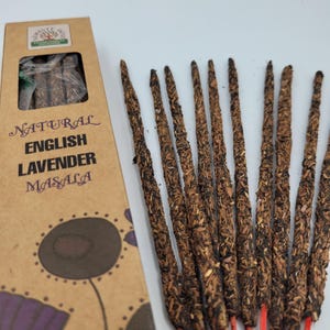 Op de afbeelding: Een doos met natuurlijke Engelse Lavendel Masala wierookstokjes. De doos is bruin met een bloemmotief en de tekst "NATURAL ENGLISH LAVENDER MASALA" erop gedrukt. De wierookstokjes zijn bruin en hebben een ruwe textuur.