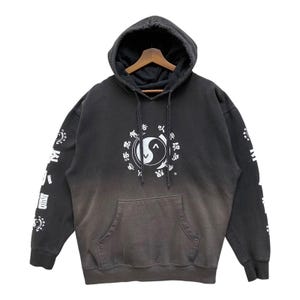 May include: Dark grey hoodie with a front pocket and a hood. The front features a white Yin Yang symbol surrounded by text. White text is also printed on the sleeves. The hoodie has a faded, distressed appearance.