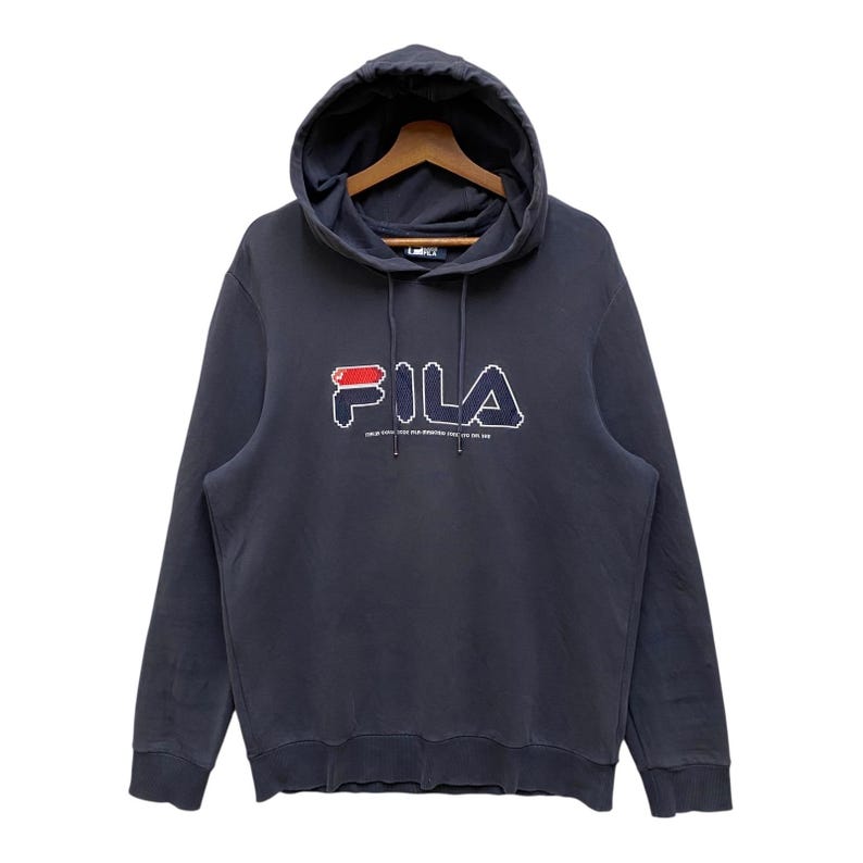 May include: A navy blue hooded sweatshirt with the brand name "FILA" in a pixelated design across the chest. The logo features red and white accents. Below the logo is the text "SINCE 1911". The sweatshirt has a drawstring and a hood.