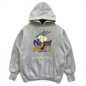 Peut inclure: Un sweat à capuche gris chiné avec une illustration du personnage Snoopy. Le texte indique FROM THE WORLD FAMOUS COMIC STRIP BY CHARLES M. SCHULZ, SNOOPY et SINCE 1950. Le sweat possède une poche kangourou sur le devant et des manches longues.