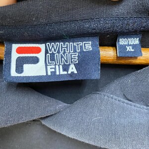 May include: Close-up of a navy blue garment tag with the text "WHITE LINE FILA" in white block letters. The tag also features the FILA logo in red and white. The size is XL.