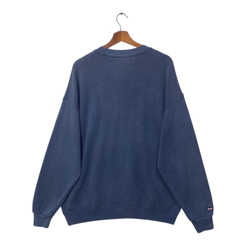 Op de afbeelding: Een marineblauw sweatshirt op een houten hanger. De top met lange mouwen heeft een ronde hals en een vervaagde uitstraling. Het merklogo is zichtbaar op de mouw. Het kledingstuk is gemaakt van een zachte stof.