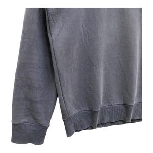 May include: A close-up shot of a faded blue sweatshirt. The garment features ribbed cuffs and hem. The fabric has a soft, textured appearance. The sleeve is visible, highlighting the cuff detail. The overall style is casual and comfortable.