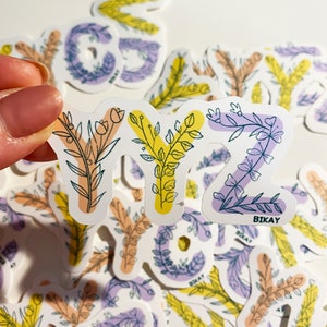 May include: A collection of floral alphabet stickers. The stickers feature the letters Y and Z, with a Y in orange and yellow, and a Z in purple. The letters are decorated with botanical illustrations and the brand name "BIKAY".