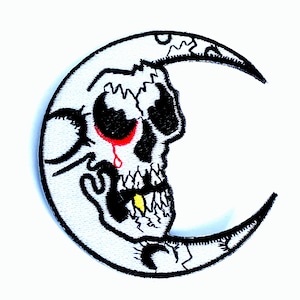 May include: Embroidered patch featuring a white crescent moon with a skull design. The skull has black eye sockets, a red tear, and a yellow tooth. The patch has black outlining and is on a white background.