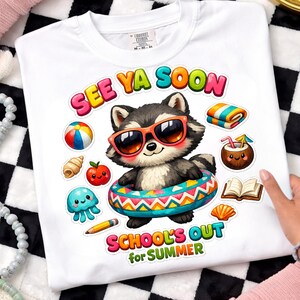 May include: White t-shirt with a colorful graphic of a raccoon wearing sunglasses and an inner tube. The text "SEE YA SOON" and "SCHOOL'S OUT for SUMMER" are displayed above and below the raccoon, along with other summer-themed illustrations.