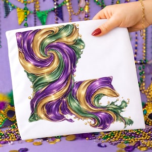 Puede incluir: Cojín cuadrado blanco con un diseño colorido del estado de Luisiana. El diseño es un remolino de morado, verde y dorado, que recuerda el tema del Mardi Gras. El cojín lo sostiene una persona con una pulsera dorada y esmalte de uñas rojo.