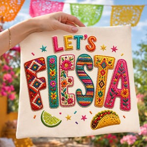 Può includere: Un cuscino color crema con le parole ricamate "LET'S FIESTA" in colori vivaci. Il design include una fetta di lime, un taco e accenti di stelle. Il cuscino è tenuto da una persona.