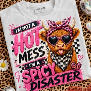 Può includere: Una t-shirt bianca con l'illustrazione di una mucca Highland marrone che indossa una fascia rosa leopardata, occhiali da sole a forma di cuore e una bandana a scacchi bianchi e neri. Il testo recita: I'M NOT A HOT MESS I'M A SPICY DISASTER.