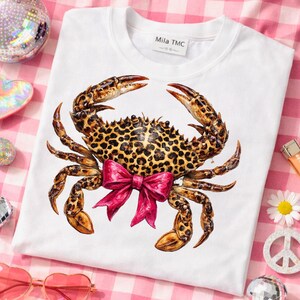 May include: White crew neck sweatshirt featuring a detailed crab illustration with a leopard print pattern and a bright pink bow. The crab design is centered on the front of the shirt. The brand name "Mila TMC" is printed on the tag.