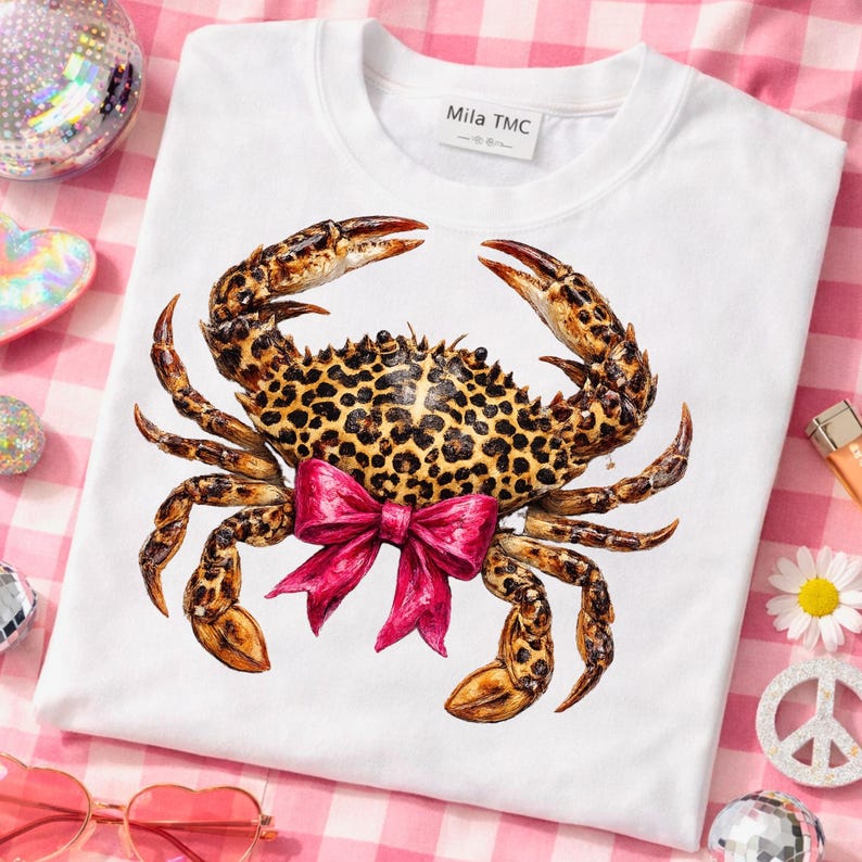 May include: White crew neck sweatshirt featuring a detailed crab illustration with a leopard print pattern and a bright pink bow. The crab design is centered on the front of the shirt. The brand name "Mila TMC" is printed on the tag.