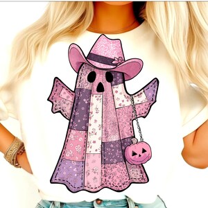 Puede incluir: Camiseta blanca con un diseño de fantasma de patchwork. El fantasma lleva un sombrero de vaquero rosa y una bolsa con forma de calabaza rosa. El patchwork incorpora patrones florales en tonos rosas y morados.