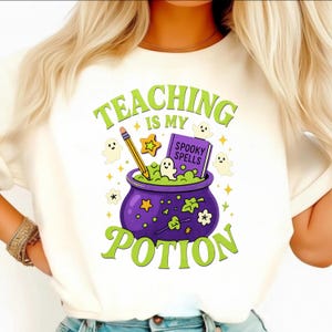 Puede incluir: Camiseta blanca con un diseño de Halloween. El diseño presenta un caldero morado con una poción verde burbujeante, un lápiz, un libro titulado "Spooky Spells" y el texto "Teaching is my Potion."