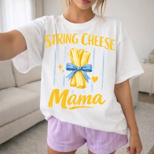 May include: White t-shirt with a yellow and blue graphic. The design features the words "STRING CHEESE Mama" with an illustration of string cheese tied with a blue bow. The shirt is paired with purple shorts.