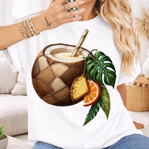 May include: White t-shirt featuring a detailed illustration of a coconut cocktail. The drink is garnished with pineapple, orange slices, and tropical leaves. The coconut is brown and tan, with a straw. The overall theme is tropical and summery.