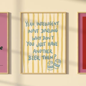 May include: A framed print with the text "Yeah, intelligent input darling, why don't you just have another beer then?" in blue. The background has vertical yellow stripes. Two beer cans are at the bottom.
