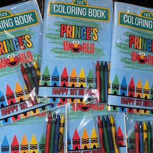May include: A set of three coloring books featuring a Sesame Street character, Elmo, with the text "Prince's World" and "Happy 1st Birthday". Each book comes with a pack of crayons.