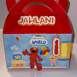 May include: Red party favor box with the name "Jahlani" in white letters. The box features a Sesame Street theme with Elmo, balloons, and the text "Jahlani's World". A large number "1" is also visible.
