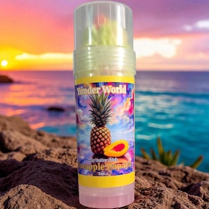 May include: A body butter stick with a label featuring a pineapple and papaya illustration. The label reads "Yonder World" and "pineapple papaya". The background shows a sunset over the ocean.