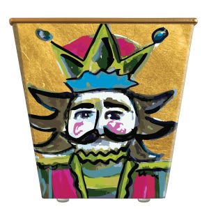 May include: A square-shaped container featuring a stylized illustration of a nutcracker figure against a metallic gold background. The nutcracker has a green crown, a blue brim, a white face with pink cheeks, and a black mustache.