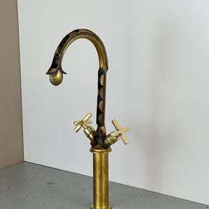 May include: A gold-toned faucet with a black and gold patterned spout and two cross-shaped handles.