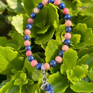 Op de afbeelding: Een armband gemaakt met roze en blauwe edelsteen kralen. De armband heeft een zilveren bedel met de tekst "made with love".