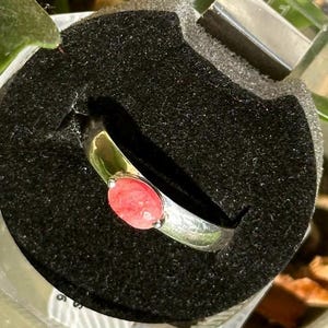 Op de afbeelding: Een zilveren ring met een roze ovale edelsteen in het midden.