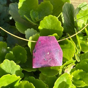 Op de afbeelding: Een roze edelsteen hanger aan een gouden ketting. De edelsteen heeft een unieke vorm met een getextureerd oppervlak.