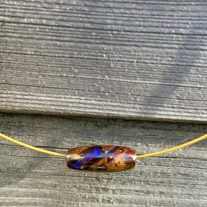Op de afbeelding: Een ketting van bruine, blauwe en gouden glazen kralen met een gele koord.