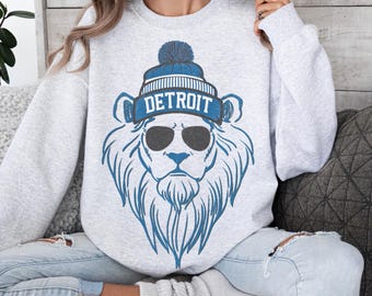 May include: A gray sweatshirt with a blue lion wearing a blue and white hat that says "DETROIT" on it. The lion is wearing sunglasses.