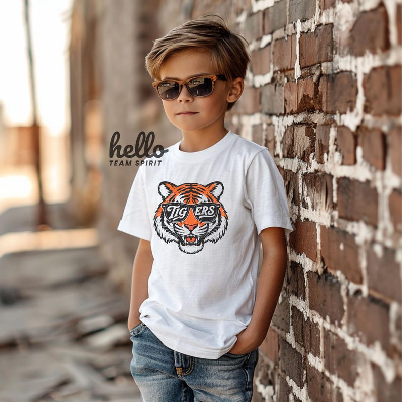 Peut inclure: Un t-shirt blanc avec un motif de tigre portant des lunettes de soleil et le mot "Tigers" sur les lunettes. Le t-shirt porte &eacute;galement le texte "hello TEAM SPIRIT" imprim&eacute; en haut &agrave; gauche.