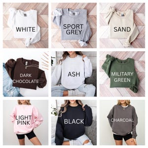 May include: A collection of nine crewneck sweatshirts in various colors. Colors include white, sport grey, sand, dark chocolate, ash, military green, light pink, black, and charcoal. Each sweatshirt has the color name printed on it.