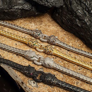 Puede incluir: Cuatro pulseras de plata y negro con cabeza de pantera con detalles de diamantes pavé. Las pulseras están dispuestas en fila sobre una superficie texturizada.