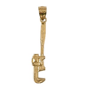 May include: A gold pendant shaped like a pipe wrench, featuring a textured handle and a movable-style jaw mechanism. The piece has a polished metallic finish and includes a small integrated bail at the top for attachment to a chain or necklace.