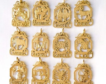 Puede incluir: Doce colgantes de color dorado con los signos del zodíaco, cada uno con un símbolo astrológico diferente. Los colgantes están dispuestos en dos filas de seis, con los signos en orden de Aries a Piscis.