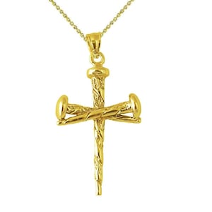May include: A gold-colored pendant necklace featuring a cross design made of nails. The cross has a textured surface and is suspended from a delicate gold chain. The pendant is a religious symbol.