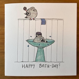May include: A greetings card featuring a hand-drawn illustration of two birds. One bird is perched above a bird bathing in a teal bird bath. The text "HAPPY BATH-DAY!" is written below the illustration.