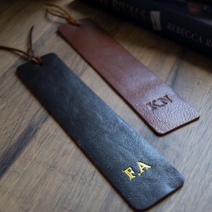 May include: Two leather bookmarks with gold lettering. The bookmark on the left is black with the initials "F.A." The bookmark on the right is brown with the initials "K.Y."